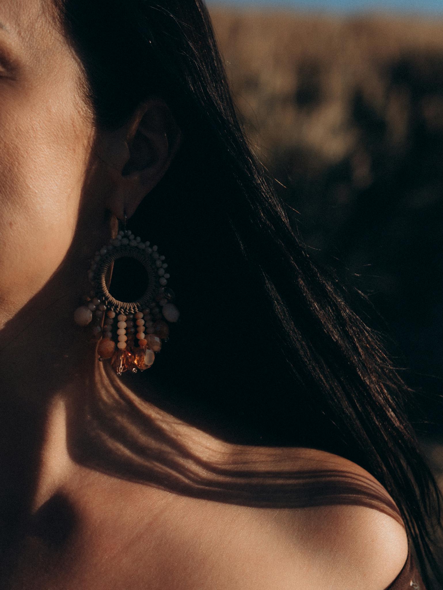 Close-up shot highlighting a woman's handmade beaded earring in warm light.